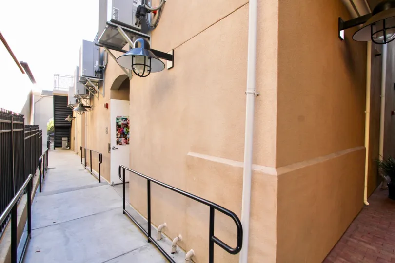 A pathway next to a peach color building with some AC equipment on the walls in MarketWalk, San Marcos, CA