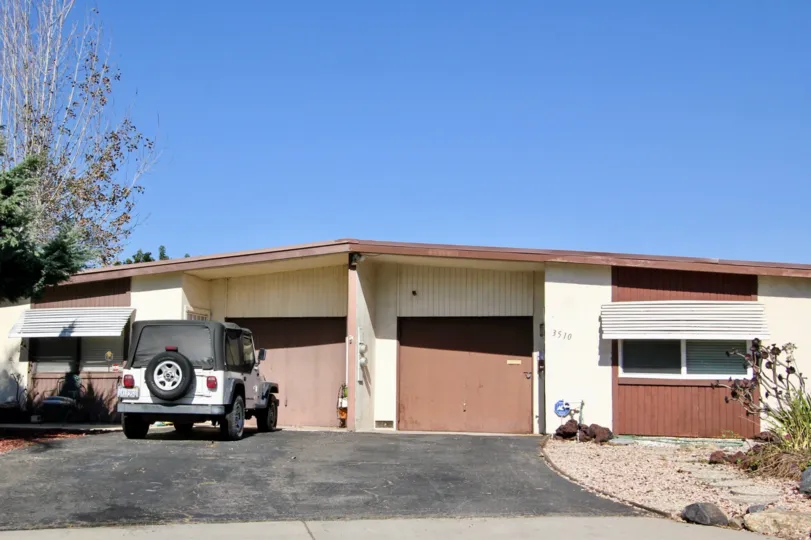 A house with two garage doors and trees in the bacak during a sunny day in San Marcos Manor, San Marcos, CA