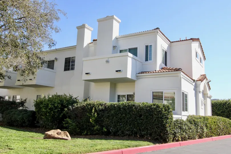 Two story white home with a large stone in it's yard inside Villa Aspara at San Marcos CA