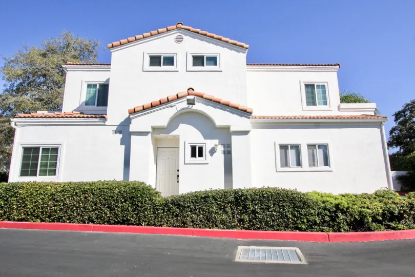Two story white building with a white door near hedge inside Villa Aspara At San Marcos CA