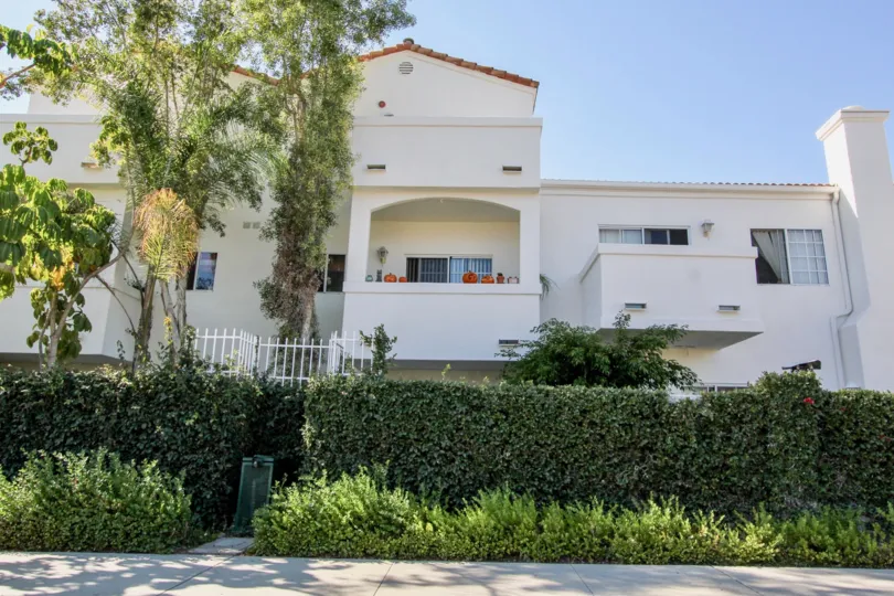 Three story white building with many trees inside Villa Aspara at San Marcos CA