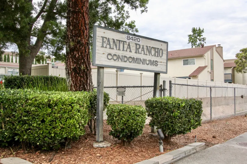 A sign stating 8420 Fanita Rancho Condominiums sitting next to nicely cut bushes and a gate