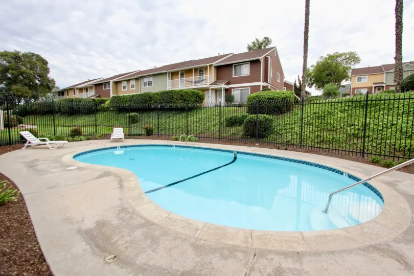 A pool with a concrete patio and lawn chairs for sitting in Pepperhill Townhomes