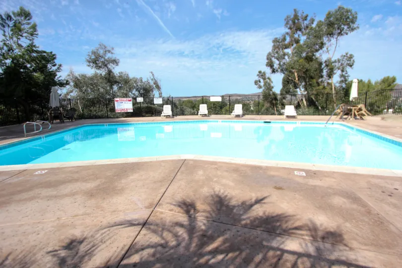 Swimming pool surrounded by black fence and trees and a sunny day in the Riderwood Terrace community in Santee, Californina
