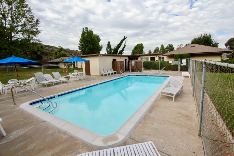 A sunny day poolside in the area of Sunset Greens, lawn chairs, ladder, fence, umbrella
