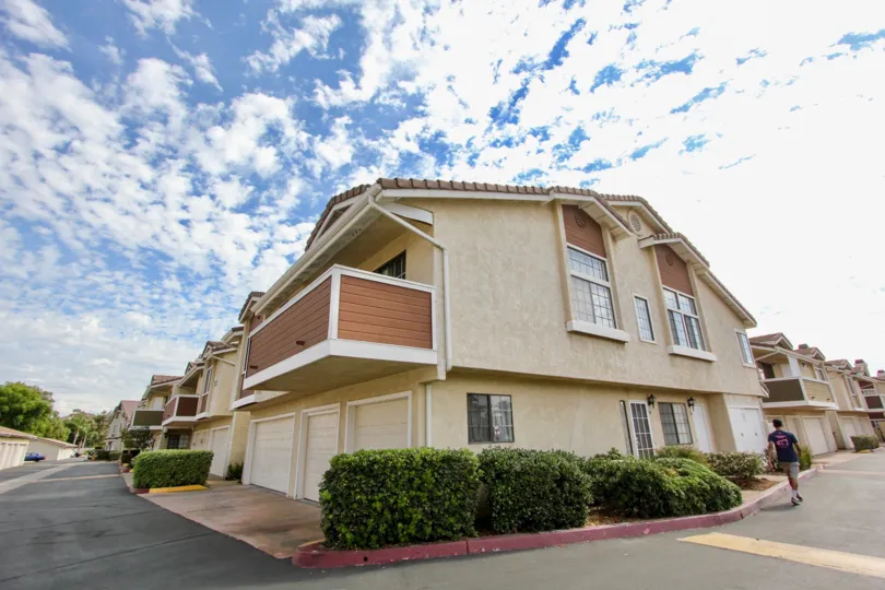 A shrub lined corner intersection and view of a balcony at a home in The Lakes neighborhood in Santee, California