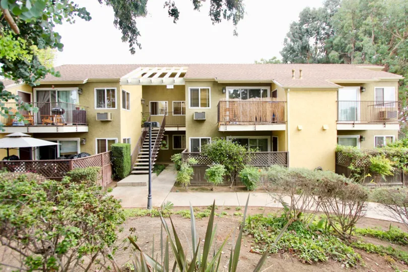 Spiky plants and dry bushes sit in a garden across form a yellow two story apartment building at Canyon Villas in Spring Valley California