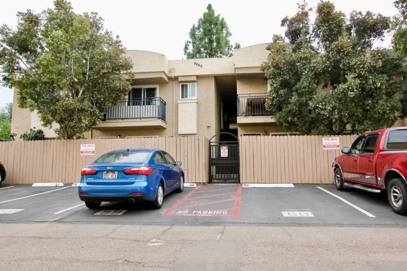 View of assigned parking stalls, mature trees, and units with wooden privacy fences and wrought iron gate in Spring Valley