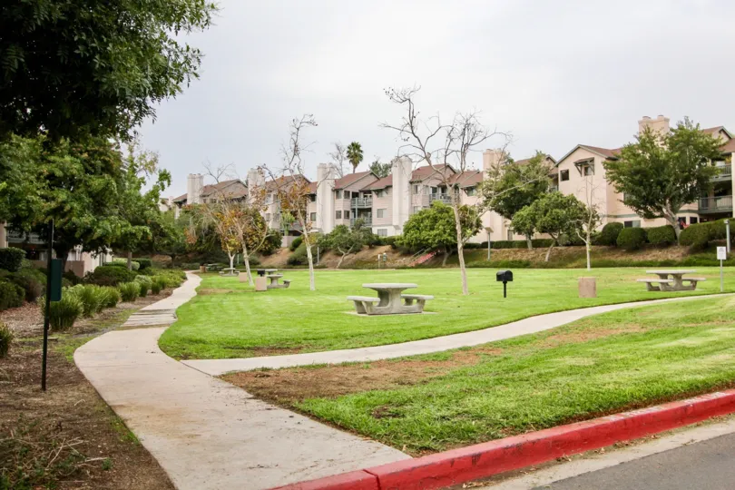 Large community park area with stone picnic tables and concrete walkways ringed by trees and shrubs at Ranchwood Park
