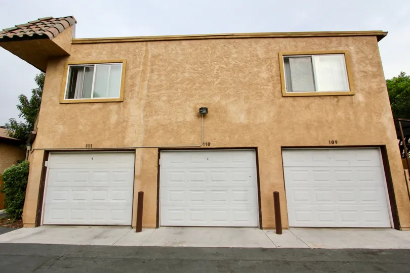 The exterior of a three-car garage in Spring Valley, California in the community of San Remos Villas. The exterior of the garage is brown with two windows and the garage numbers are 111, 110, and 109.