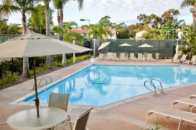 A SUNNY DAY IN THE LA JOLLA VILLAGE PARK WITH SWIMMING POOL, CHAIRS, UMBRELLA, TREES.