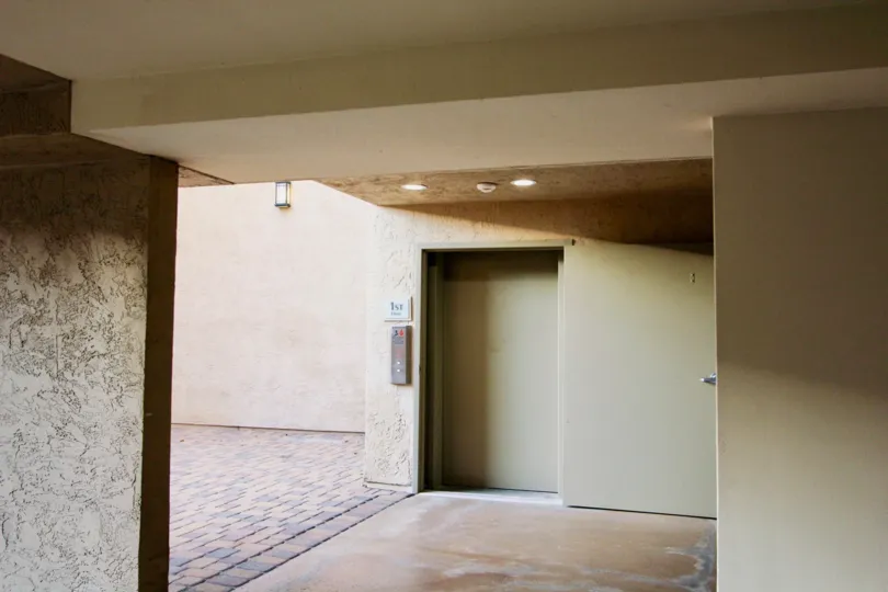 Inside of a bulding with a door, elevator, and wide open area to the left, located in Villa Vicenza, University City, California.