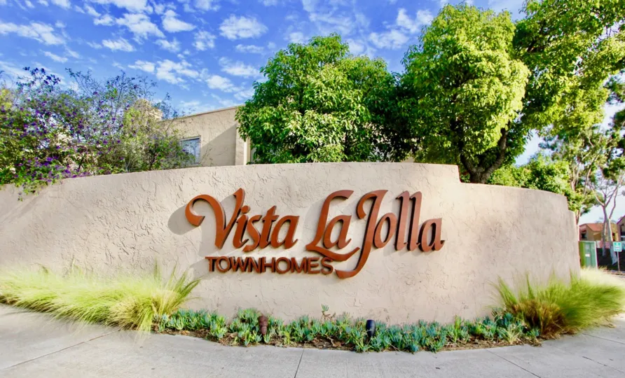 A sign for Vista La Jolla Townhomes with trees in the background.