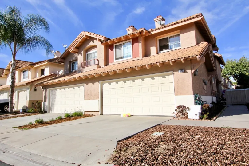 A two-story house with a large garage door and a palm tree on the side during a sunny day in California Villas, Vista, CA