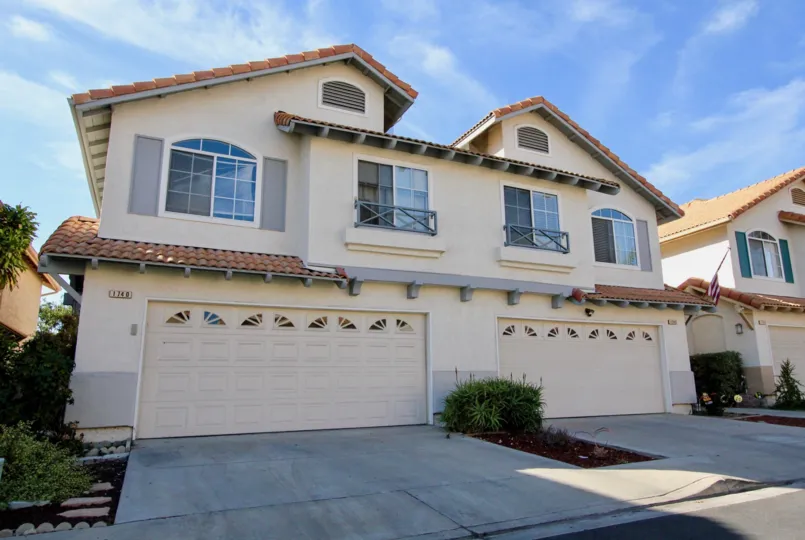 A duplex two-story house with big garage doors and some bushes during a sunny day in California Villas, Vista, CA