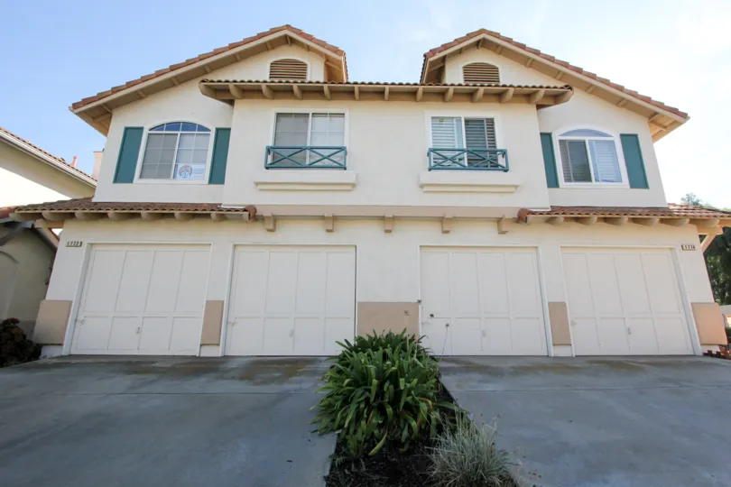 A sunny day in the area of California Villas, Garage, windows, parking lit, bushes