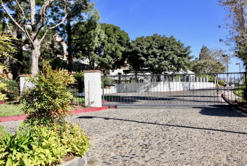 A black gate facing to a street with some large trees in the background during a sunny day in Copper Hill, Vista, CA