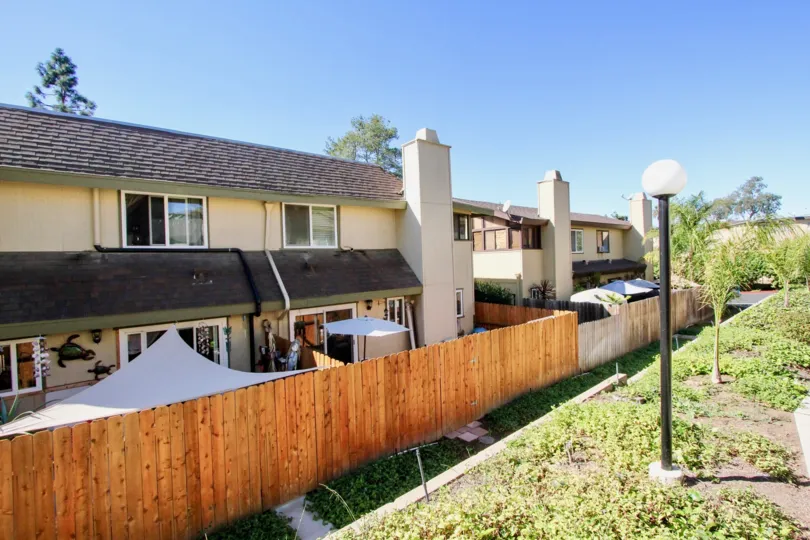 A row of back yards from various houses with a wooden fence and some plants and lamps on front during a sunny day in Marlin Terrace, Vista, CA