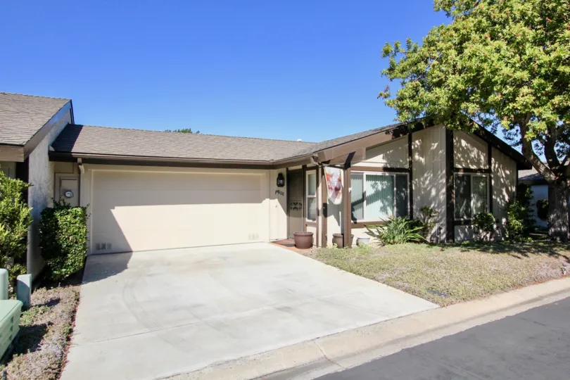 A house with a large driveway and garage door and a lawn with some bushes and a tree during a sunny day in Nob Hill, Vista, CA