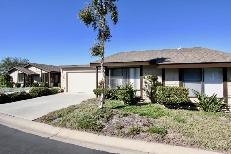A house with a large driveway, a lawn with some bushes and a tree during a sunny day in Nob Hill, Vista, CA
