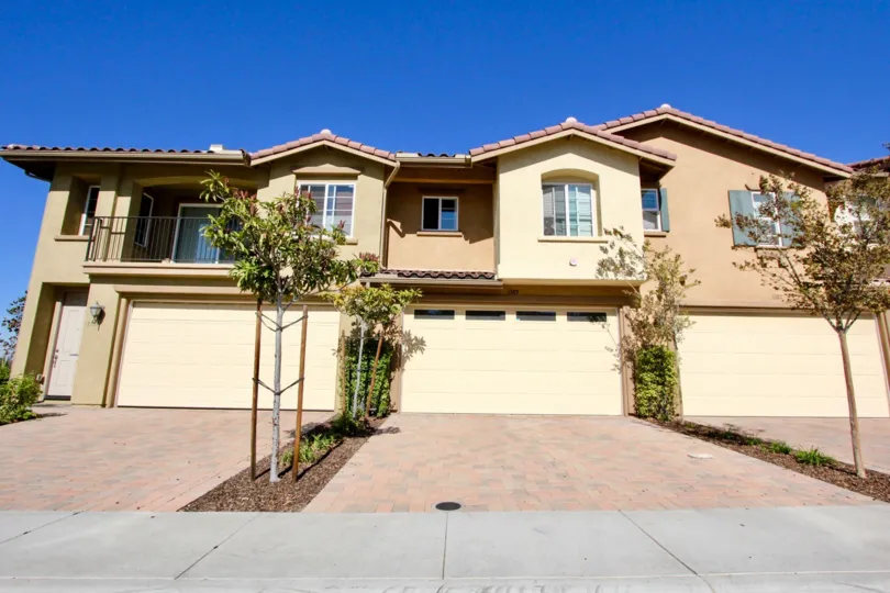 A large villa with a balcony, a large porche and garage and a couple of trees in the Oak Drive Villas Community in Vista, California
