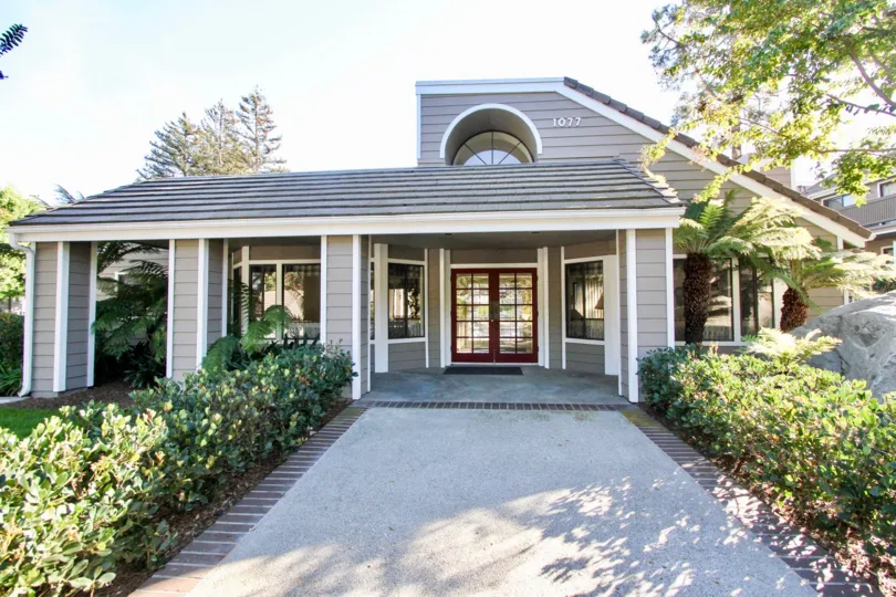 The villa in the Shadowridge Aspens has glass doors and windows with plants on both sides of the pathway