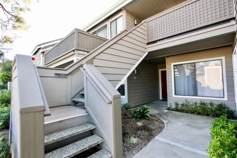 A house with an outdoor staircase and some bushes during a sunny day in Shadowridge Aspens, Vista, CA