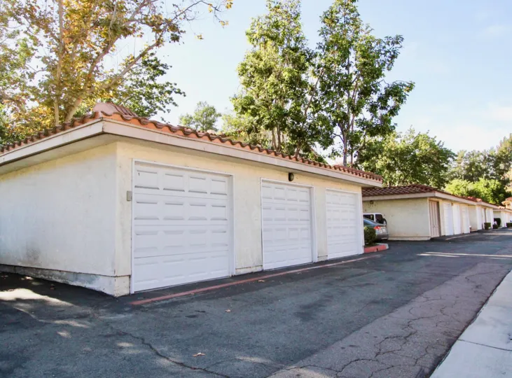 A row of garage doors along a driveway with some big trees in the back during a sunny day in Shadowridge Glen, Vista, CA