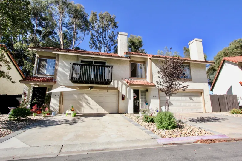 A big yellow house with a large driveway and some trees in the back during a sunny day in Vista Knolls, Vista, CA