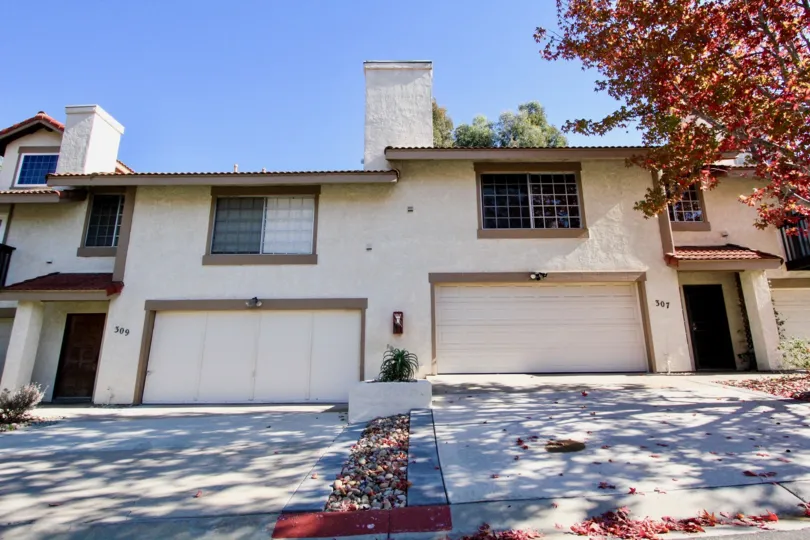 Two yellow houses with large garages and a red leaf tree on the side during a sunny day in Vista Knolls, Vista, CA