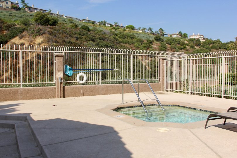 there is a swimming pool and it is a sunny day and house is placed at the top and covered with trees and grasses