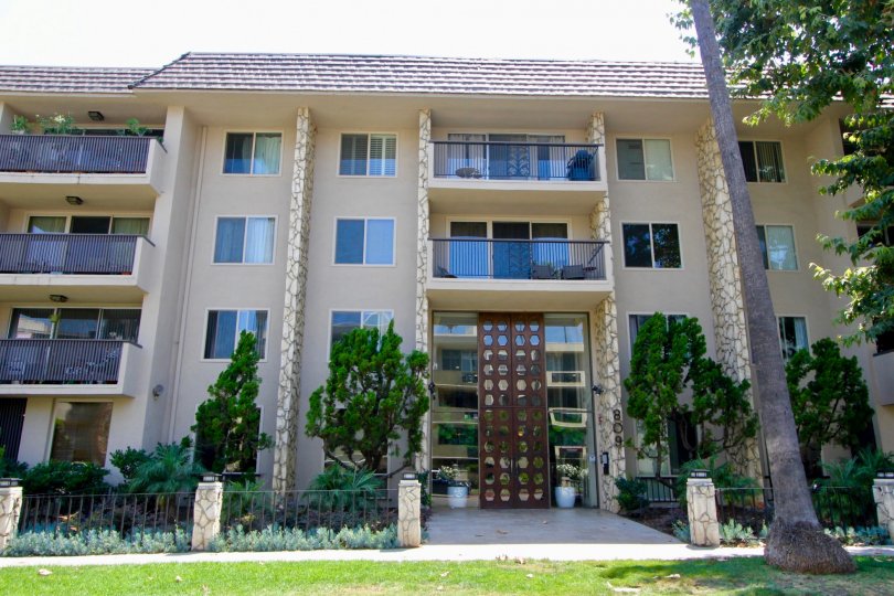 Tall 4 story apartment building with tan exterior and nice fence surrounding the garden.