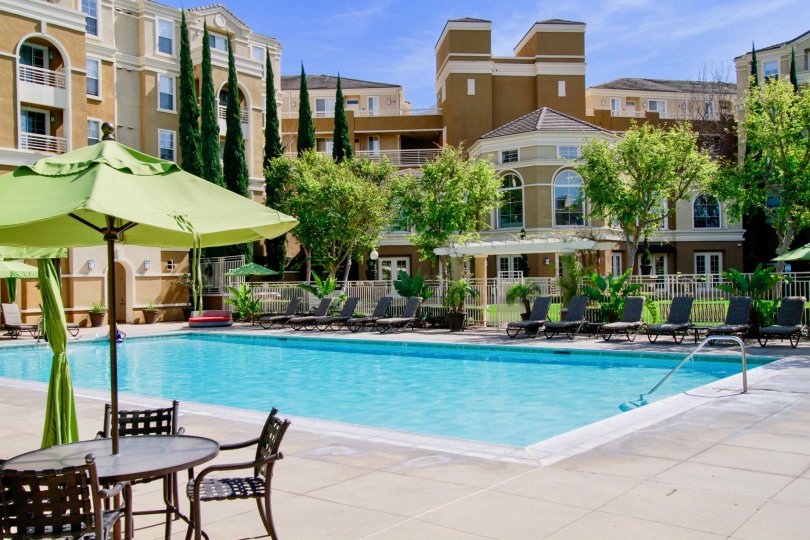 Inside the apartment in Vantage has tallest trees, swimming pool, dinning tables, seating chairs and with umbrella's