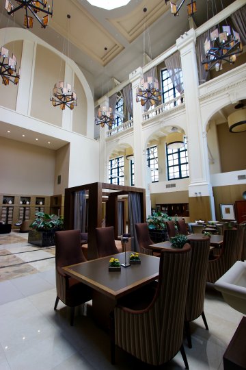 A view of the lobby of the Electra building with modern light fixtures, cathedral ceiling, and skylights over comfortable dining tables.