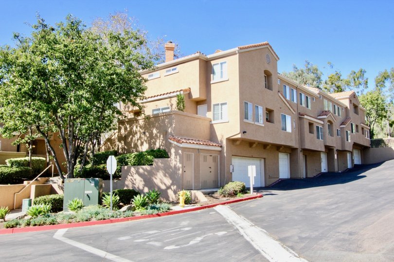 A sloped street with some houses and a tree during a sunny day at The Knolls, El Cajon, CA